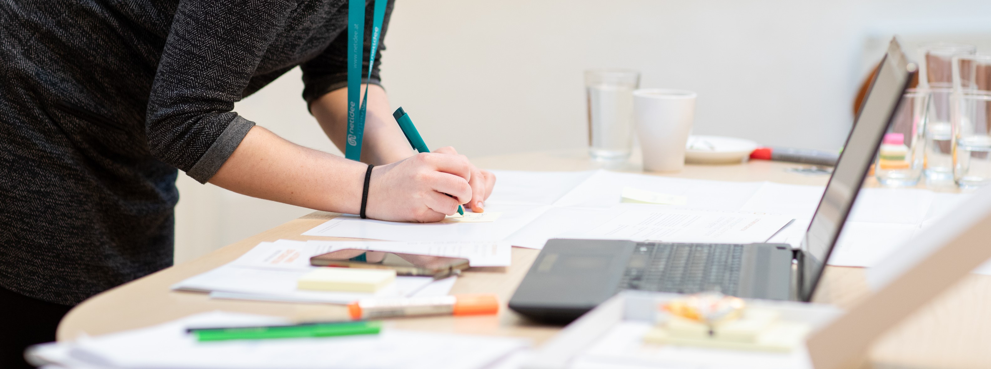 Person writing with a pen on paper next to a laptop