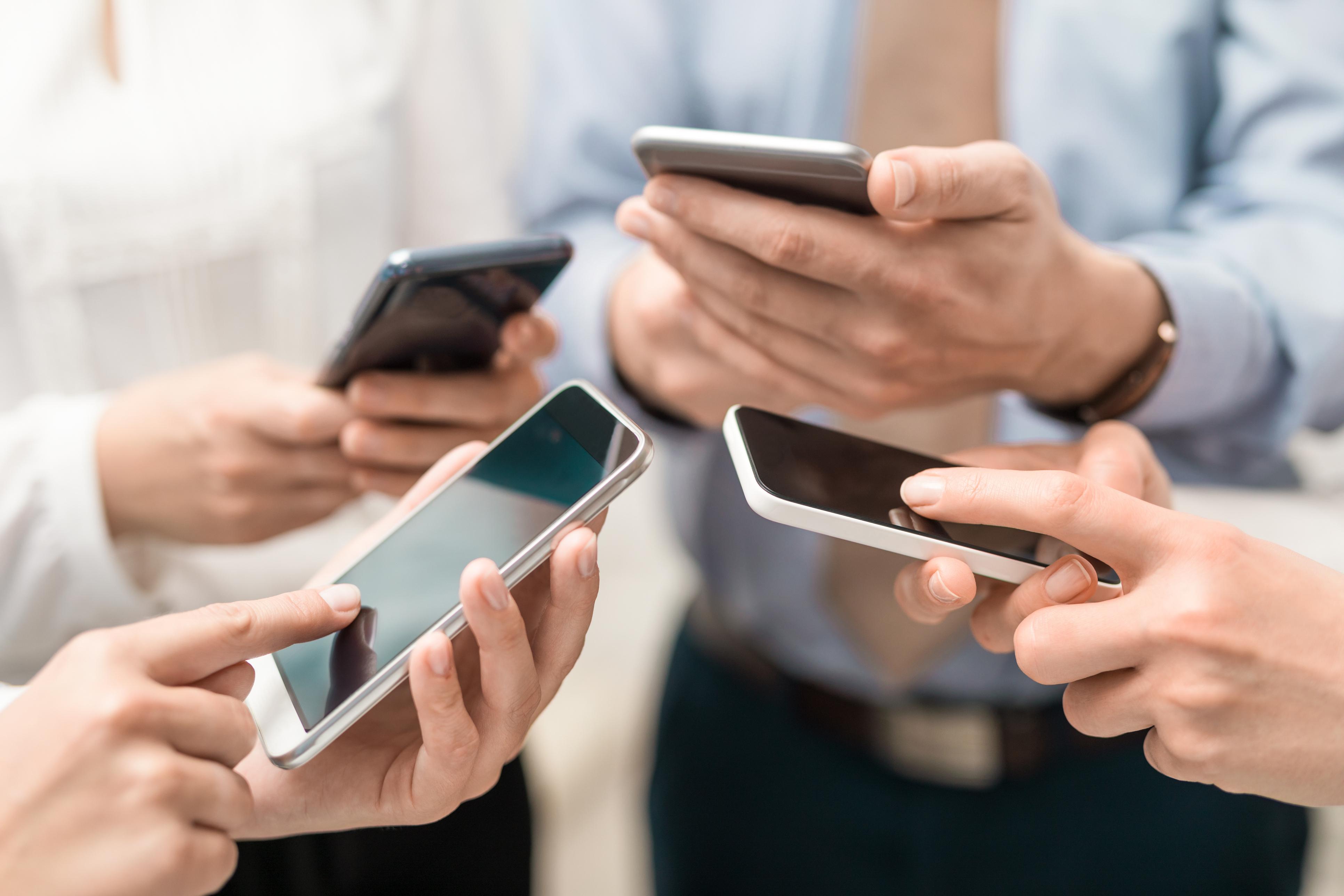 Vier Menschen halten und bedienen ihr Smartphone.