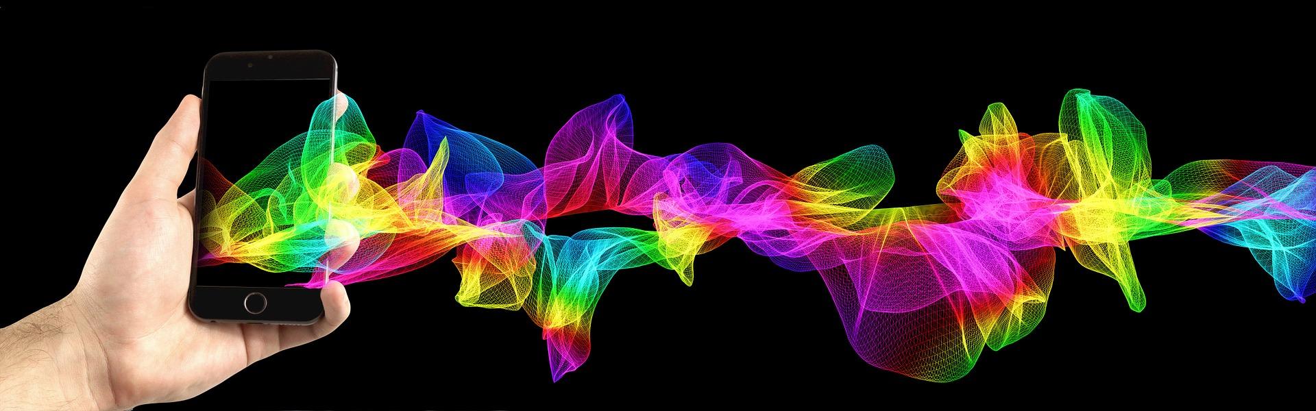 In der Abbildung ist eine Hand sichtbar, welche ein Smartphone hält. Aus dem Smartphone kommen bunte Wellen heraus.