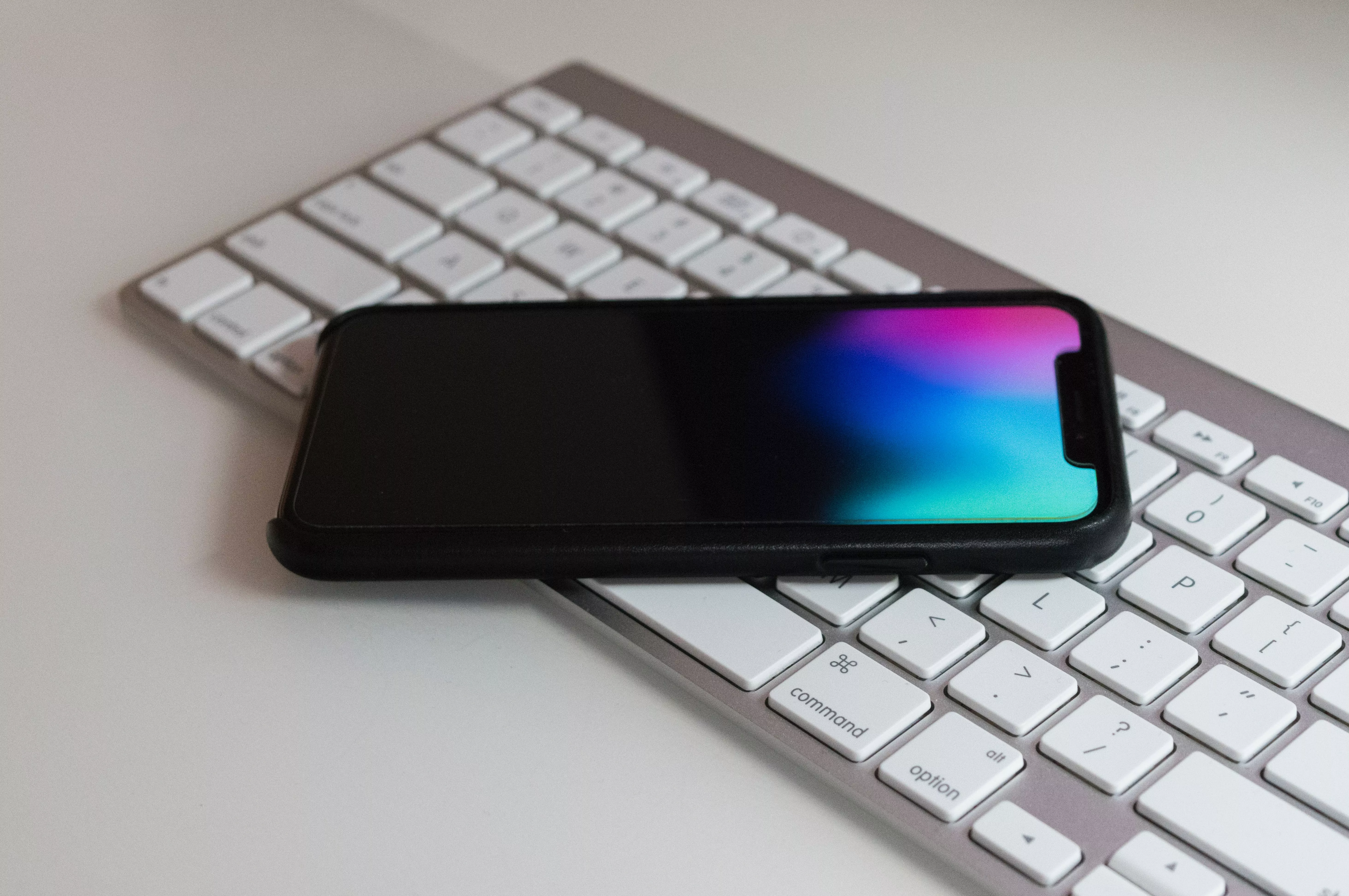 Die Abbildung zeigt eine Apple-Tastatur auf welcher ein Apple iPhone liegt.