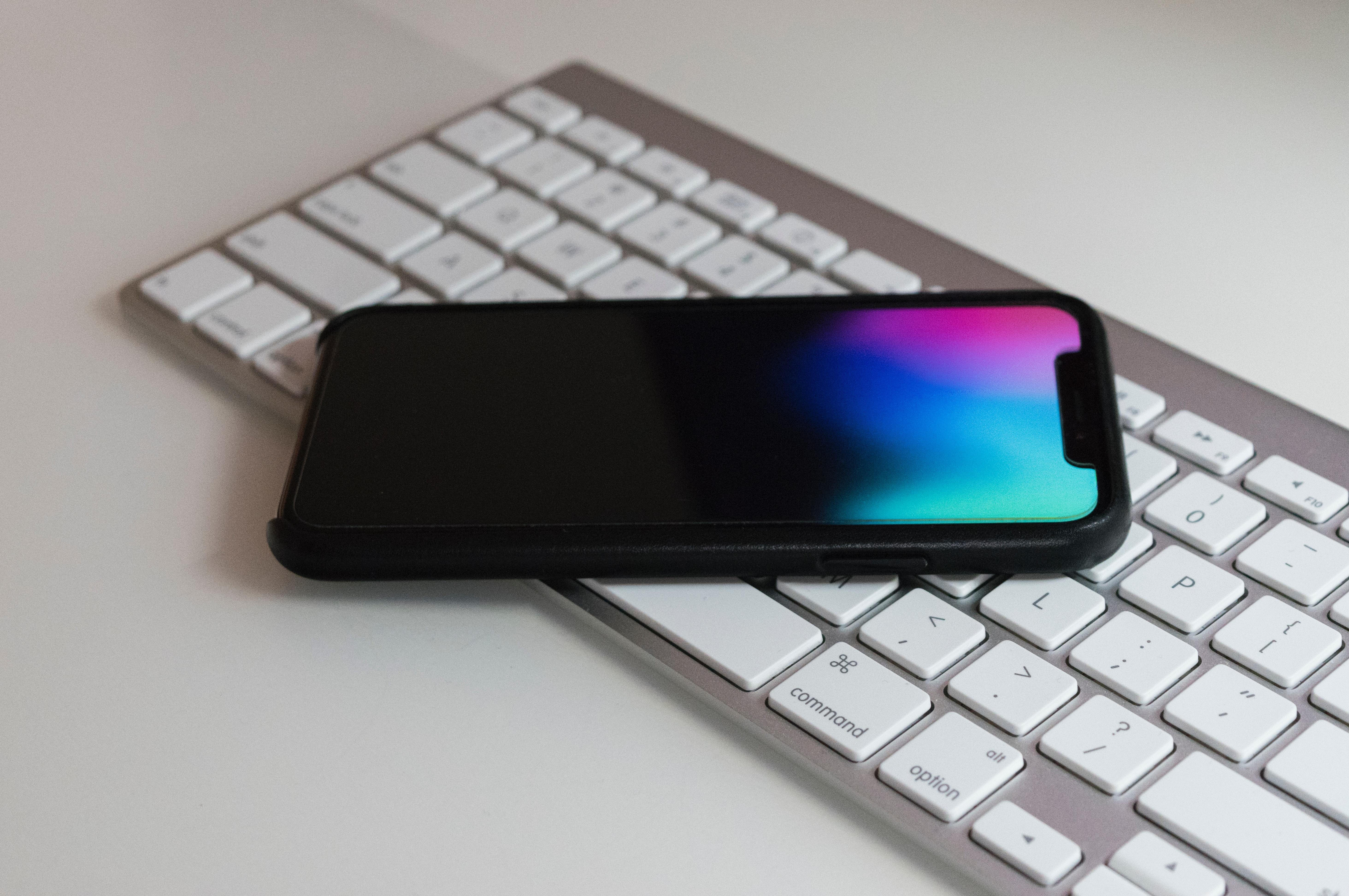 Die Abbildung zeigt eine Apple-Tastatur auf welcher ein Apple iPhone liegt.