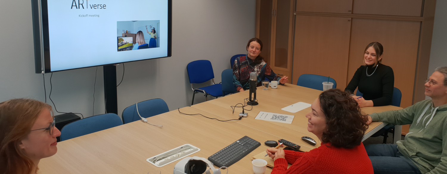 ARTverse's five team members sit around a meeting table while watching a presentation on a television screen.