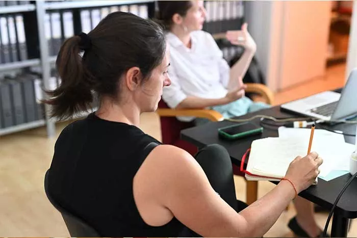 Mitarbeiterin schreibt mit. Trainerin unscharf im Hintergrund erklärt.