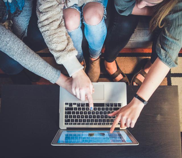 Vier Personen deuten auf einen Laptop