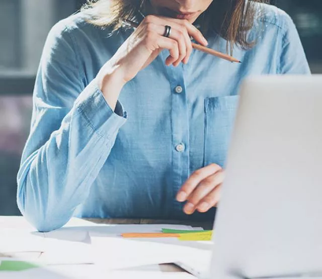 Woman looking at a laptop, holding a pencil