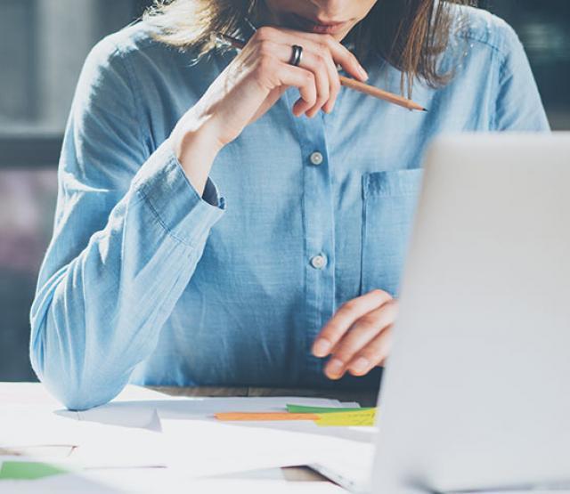 Woman looking at a laptop, holding a pencil