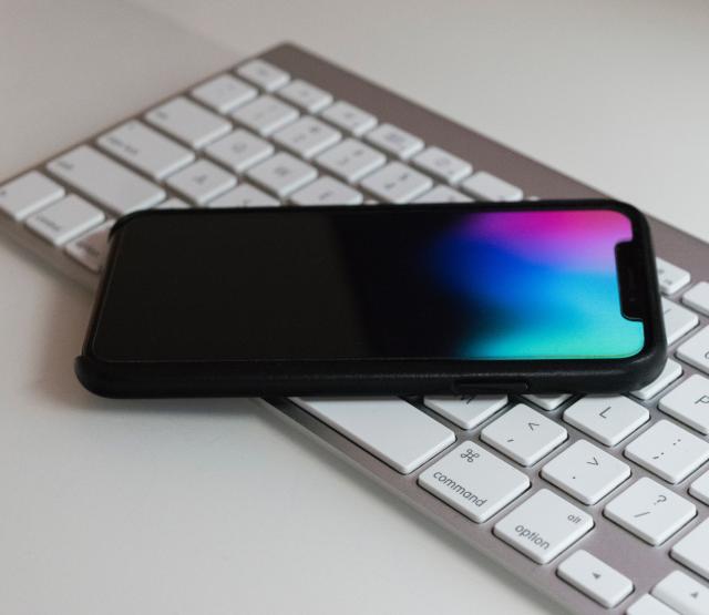 Die Abbildung zeigt eine Apple-Tastatur auf welcher ein Apple iPhone liegt.