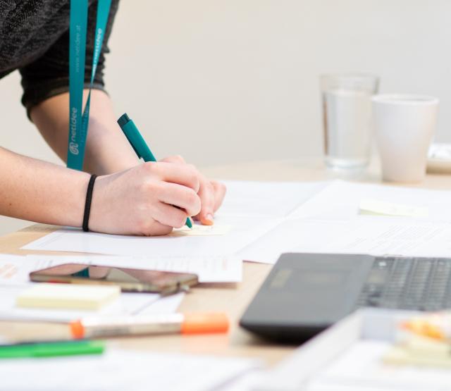 Person writing with a pen on paper next to a laptop