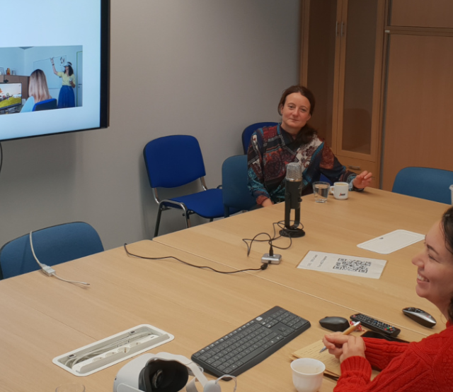 ARTverse's five team members sit around a meeting table while watching a presentation on a television screen.