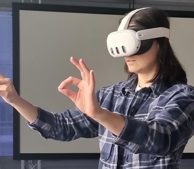 Woman wearing Meta Quest 3 virtual reality headset making pinching gestures in an office environment. 