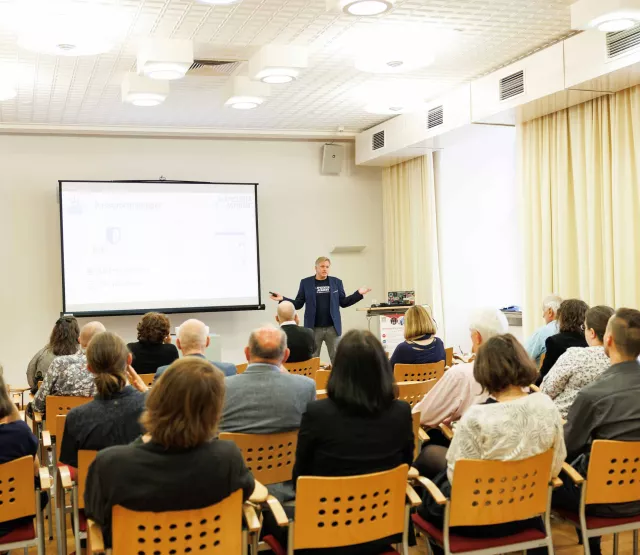 Daniel Lohninger steht vor einem Publikum am OSGS Forum in einem hellen Seminarraum und hält einen Vortrag zum Thema Datenschutz und IT-Sicherheit. Auf der Leinwand hinter ihm ist das Logo von „Bitwarden“ sowie der Schriftzug „epicenter.academy“ zu sehen. Die Zuhörer:innen verfolgen aufmerksam die Präsentation. Der Raum ist mit Holzstühlen, Deckenleuchten und großen Fenstern mit Vorhängen ausgestattet. Ein Flipchart steht ungenutzt am Rand. Copyright:Sima Prodinger