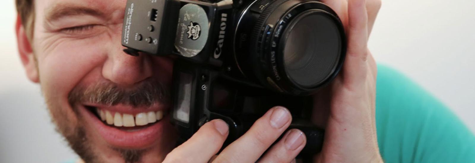 Portraitfoto von Christoph Uiberacker mit Fotoapparat vor Gesicht