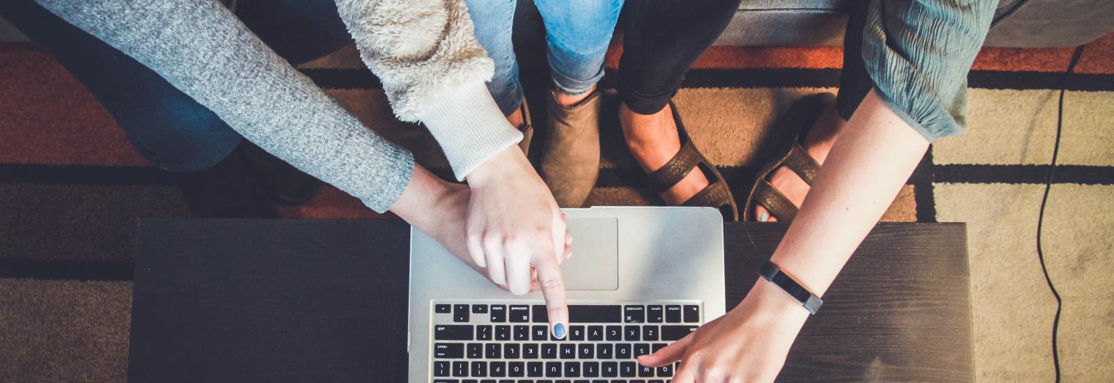 Vier Personen deuten auf einen Laptop