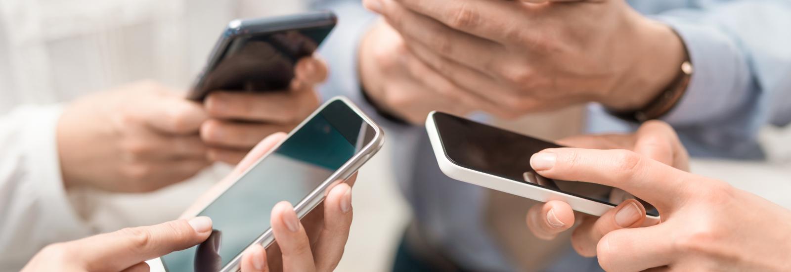 Vier Menschen halten und bedienen ihr Smartphone.