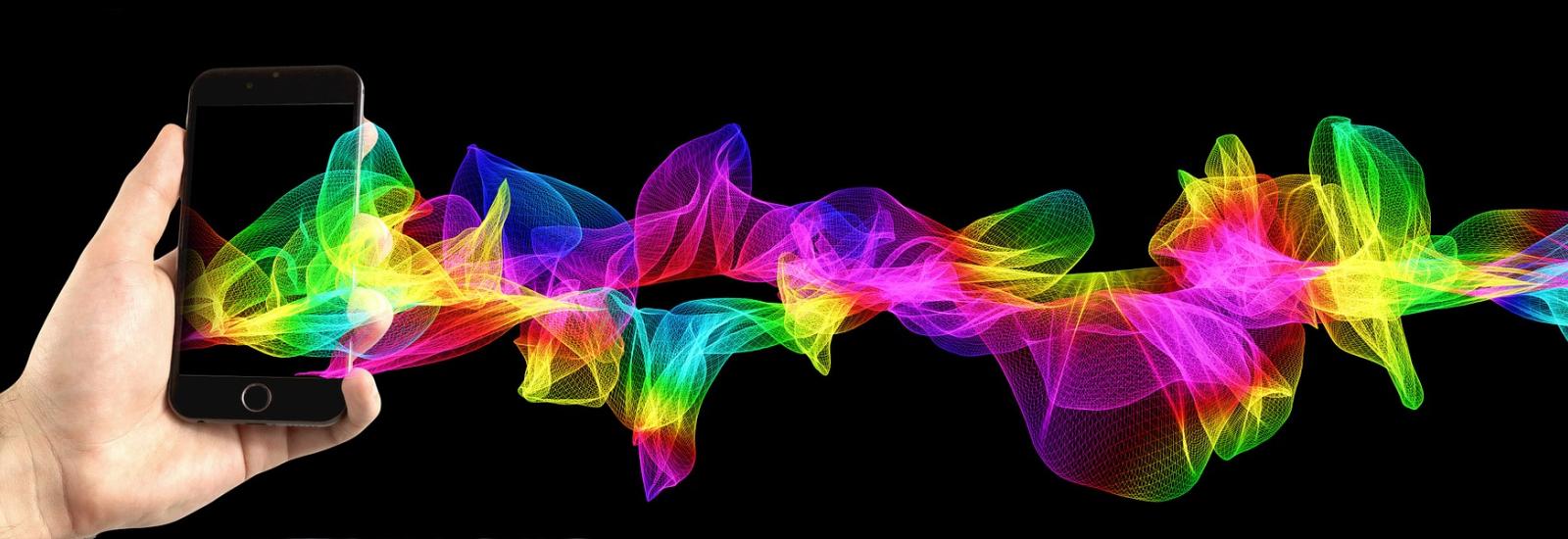 In der Abbildung ist eine Hand sichtbar, welche ein Smartphone hält. Aus dem Smartphone kommen bunte Wellen heraus.