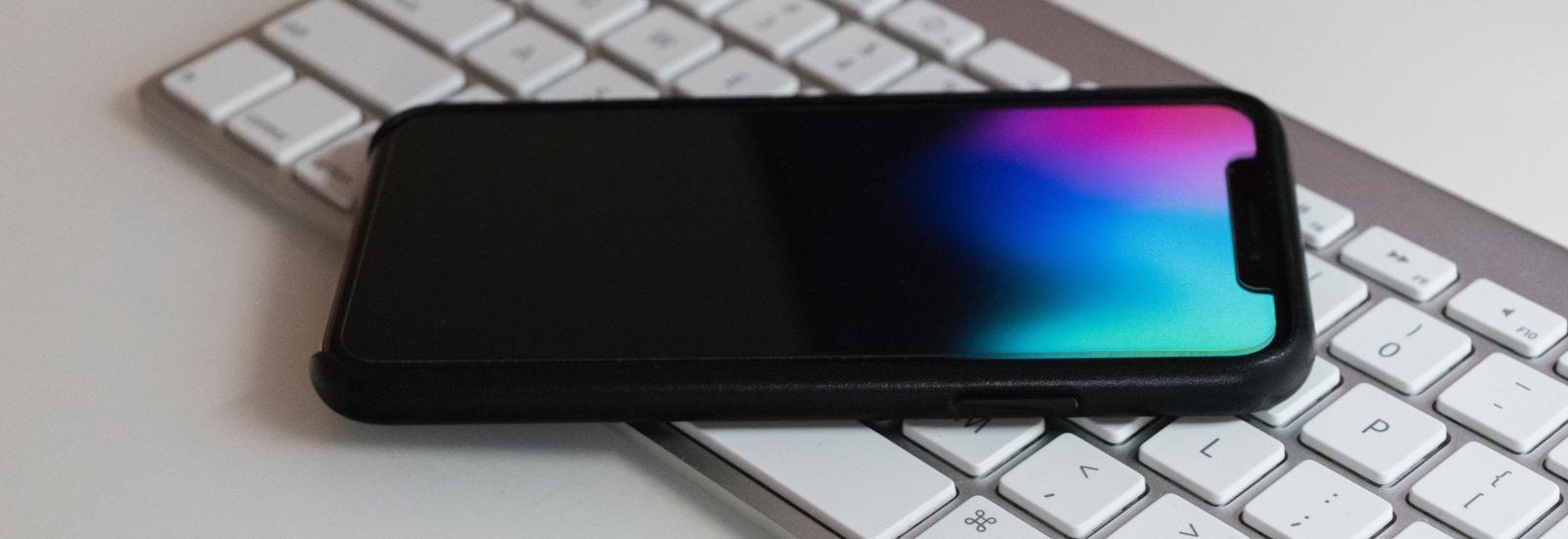 Die Abbildung zeigt eine Apple-Tastatur auf welcher ein Apple iPhone liegt.