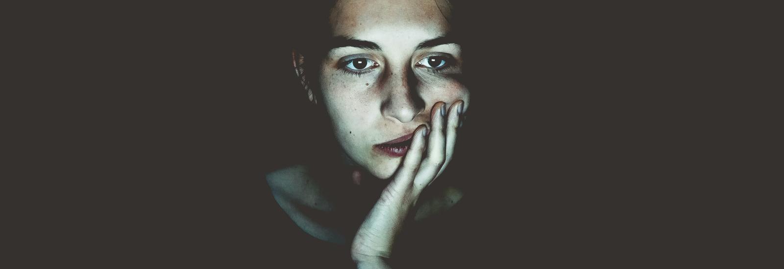 Frau starrt geradeaus - durch das bläuliche Licht in ihrem Gesicht lässt sich vermuten, dass sie auf einen Bildschirm starrt