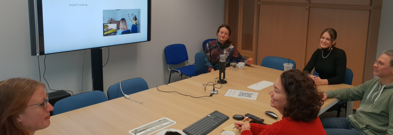 ARTverse's five team members sit around a meeting table while watching a presentation on a television screen.