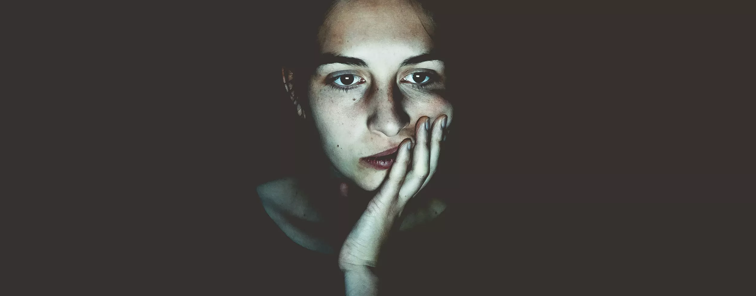 Frau starrt geradeaus - durch das bläuliche Licht in ihrem Gesicht lässt sich vermuten, dass sie auf einen Bildschirm starrt