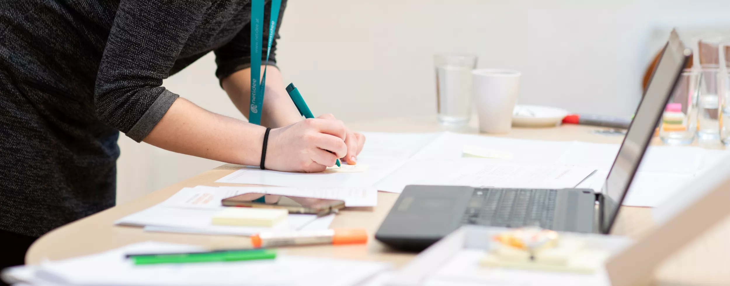 Person writing with a pen on paper next to a laptop