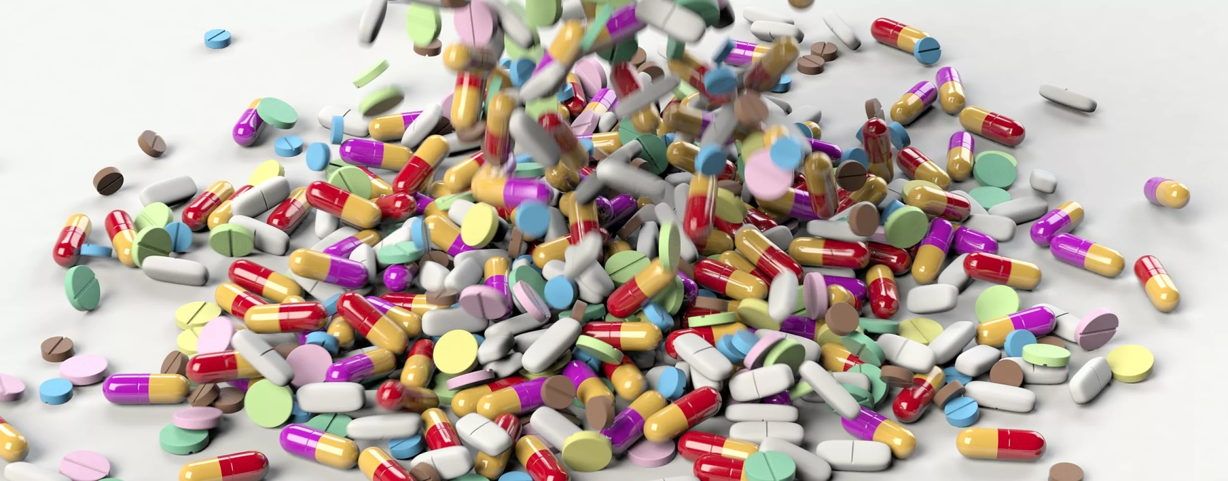 Eine große Anzahl an buten Pillen fällt auf einen weißen Untergrund.